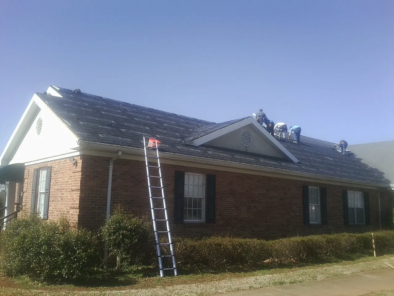 Crew tearing shingles off a brick ranch roof with a ladder set — Metal Roof Repair work by our crew in Atwater