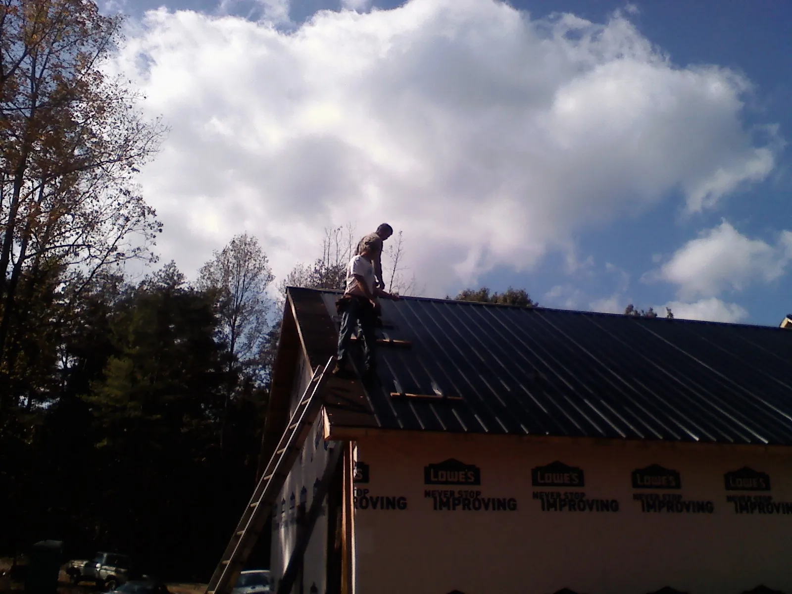 Roofer fastening dark metal panels high against a cloudy sky, from a Roof Inspection job in Atwater